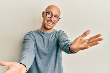 Sıradan kıyafetler ve gözlük takmış kel bir adam kameraya bakıp sarılmak için kollarını açmış gülümsüyor. Mutluluğu kucaklayan neşeli bir ifade.. 