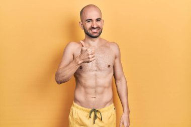 Mayo giyen genç kel adam elleriyle mutlu bir jest yapıyor. Kameraya bakıp başarıyı gösteren ifade. 