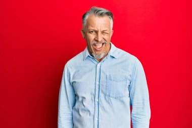 Orta yaşlı, gri saçlı, sıradan kıyafetler giyen, kameraya seksi bir ifadeyle bakan, neşeli ve mutlu yüzlü bir adam.. 