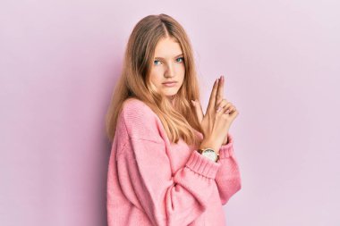 Güzel, genç, beyaz bir kız, gündelik giysiler içinde, sembolik bir silah taşıyor, el hareketleriyle cinayet silahlarıyla oynuyor, kızgın bir yüz ifadesi var. 