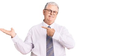 İş kıyafetleri giyen yaşlı gri saçlı adam kameraya hayret ediyor ve gülümsüyor.. 