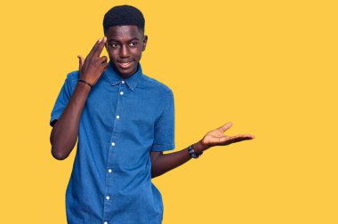 Genç Afro-Amerikalı bir adam günlük giysiler giymiş. Kafası karışmış ve avuç içi açık bir şekilde fotokopi alanı göstermekten rahatsız olmuş ve alnını işaret ediyor. Bunu bir düşün.. 