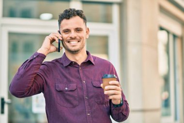 Genç İspanyol adam akıllı telefondan konuşuyor ve şehirde kahve içiyor..