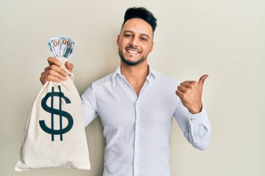 Dolarları tutan genç Arap adam başparmağını yana kaldırarak mutlu bir şekilde gülümsüyor. 