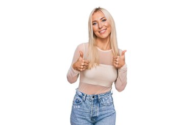 Sıradan kıyafetler giyen genç sarışın kadın. Başarı işareti yapıyor. Elleriyle olumlu jest yapıyor. Neşeli ifade ve kazanan jest. 