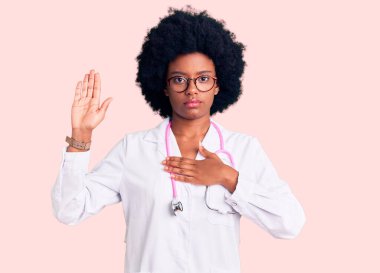 Genç Afro-Amerikan kadın doktor önlüğü ve steteskop takmış, el pençe divan yemin ederek sadakat yemini ediyor. 