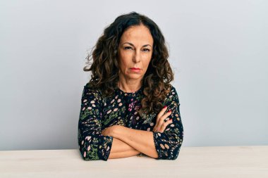 Masada sıradan kıyafetler giyen, kuşkucu ve gergin, yüzünde çapraz kollu tasvip etmeyen orta yaşlı güzel bir kadın. negatif kişi. 