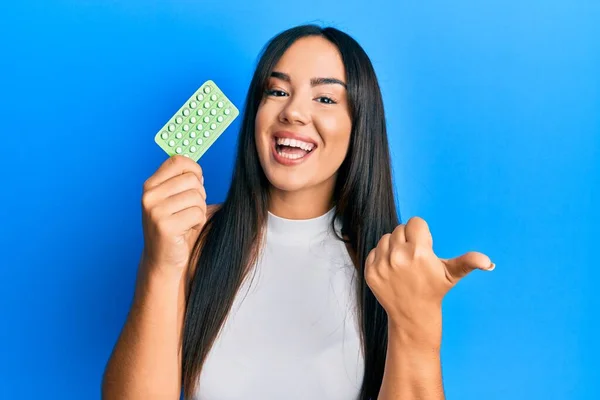 Young Beautiful Hispanic Girl Holding Birth Control Pills Pointing Thumb — Stockfoto