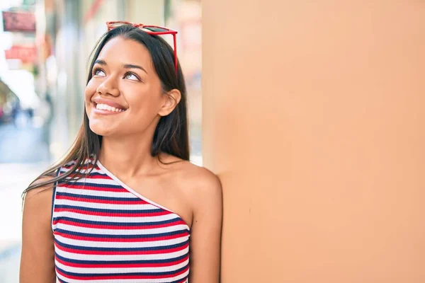 若いですラテン語の女の子笑顔幸せそうに街の壁にもたれて — ストック写真