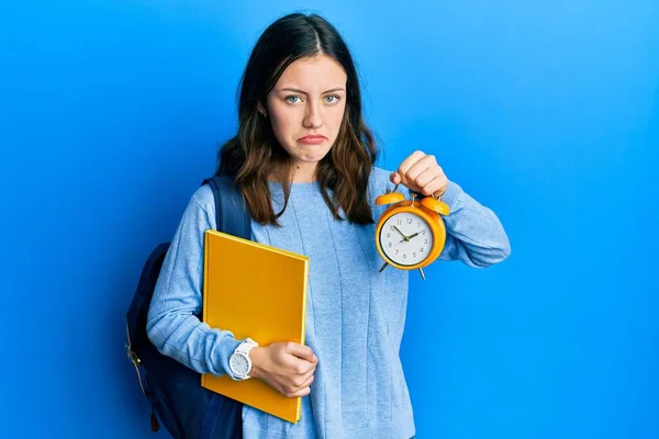 Young Brunette Student Woman Holding Alarm Clock Skeptic Nervous Frowning — Stock Photo, Image