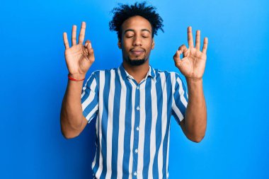 Sakallı, sıradan çizgili tişört giyen, gözleri kapalı gülümseyen, meditasyon yapan, parmaklarıyla meditasyon yapan Afrikalı genç bir Amerikalı. yoga konsepti. 