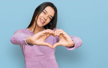 Gündelik kıyafetler giyen, aşık gülümseyen, elleriyle kalp sembolü yapan genç İspanyol kız. romantik kavram. 