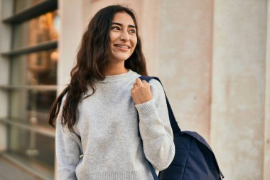 Genç ortadoğulu kız gülümseyerek şehirde mutlu mesut duruyor..