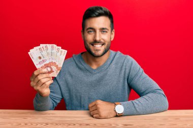 Yakışıklı İspanyol adam elinde Kolombiya pezosu tutuyor. Olumlu ve mutlu görünüyor. Kendine güvenen bir gülümsemeyle dişlerini gösteriyor. 