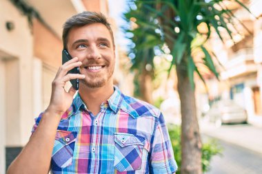 Genç beyaz adam gülümsüyor. Şehirdeki akıllı telefondan konuşuyor..