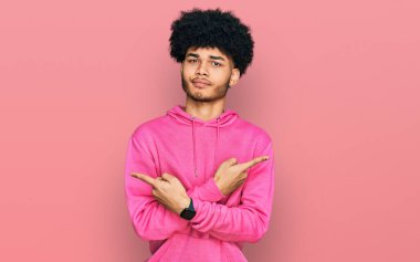 Afro saçlı, pembe tişörtlü, iki tarafı da parmaklarıyla gösteren Afro Amerikalı genç bir adam. 