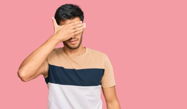 Genç ve yakışıklı bir adam, sıradan kıyafetler giyip gözlerini eliyle kapatıyor, ciddi ve üzgün görünüyor. Görme, saklama ve reddetme konsepti 