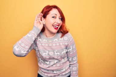 Güzel kızıl saçlı kadın, sarı arka planda ren geyiğiyle Noel süveteri giyip, sırıtarak dedikodu ve dedikoduları dinliyor. Sağırlık kavramı.