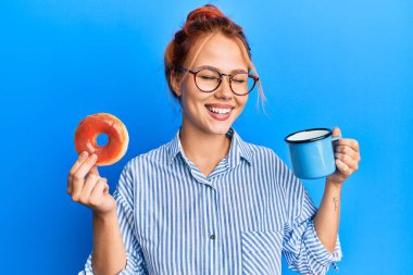 Genç kızıl saçlı kadın elinde çikolatalı çörek ve kahveyle kahvaltı yapıyor kahkahalarla kahkahalarla gülüyor.. 