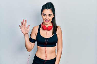 Spor kıyafetleri giyen ve kulaklık takan genç İspanyol kız beş numarayı gösterip işaret ederken kendinden emin ve mutlu bir şekilde gülümsüyor.. 