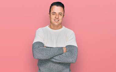 Kış süveteri giyen yakışıklı genç adam kollarını kavuşturup kameraya bakarken gülümsüyor. pozitif kişi. 