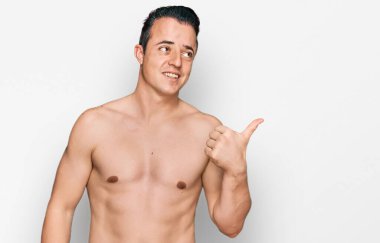 Mayo giyen yakışıklı genç adam mutlu yüzüyle gülümseyen ve başparmağıyla yan tarafı gösteren.. 