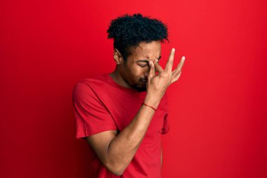 Sakallı, sıradan kırmızı tişörtlü, burnu ve gözleri ovuşturmaktan yorgun düşmüş yorgun ve başı ağrıyan Afrikalı genç bir Amerikalı. Stres ve hüsran kavramı. 