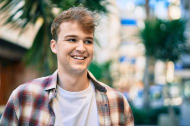 Genç beyaz adam gülümseyerek şehirde mutlu mesut duruyor..