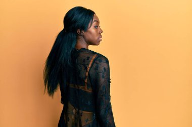 Genç Afrikalı Amerikalı kadın seksi iç çamaşırları giyiyor ve sarı arka planda ciddi ve baştan çıkarıcı bir yüzle poz veriyor.