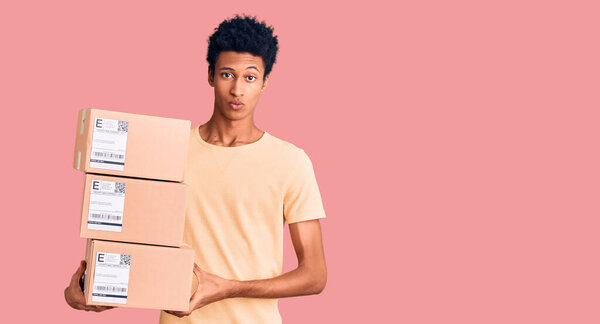 Young african american man holding delivery package thinking attitude and sober expression looking self confident 
