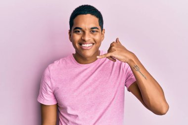 Genç, yakışıklı, pembe tişört giyen, gülümseyen, el ve parmaklarıyla telefon hareketi yapan telefonda konuşan bir İspanyol. iletişim kavramları. 