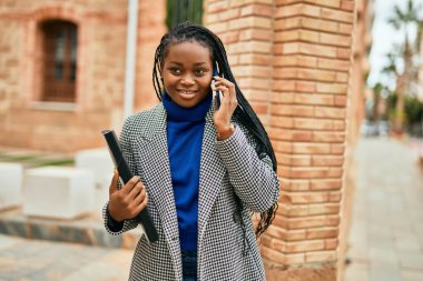 Genç afro-amerikan iş kadını gülümseyerek şehirdeki akıllı telefondan konuşuyor..