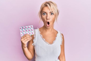 Sarışın kız elinde haplar tutuyordu. Korkmuş ve ağzı açık bir şekilde hayrete düşmüştü. 