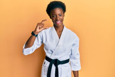 Genç Afrikalı Amerikalı kız karate kimonosu ve siyah kuşak takıyor gülümsüyor ve el hareketleriyle küçük boy işareti yapıyor ve kameraya bakıyor. ölçüm kavramı. 