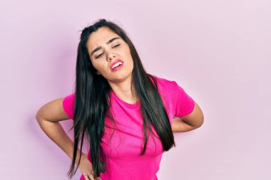 Sırt ağrısından muzdarip, sıradan pembe tişörtler giyen genç İspanyol kız elleriyle dokunuyor, kas ağrısı çekiyor. 