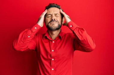 Orta yaşlı bir adam, elleri kafasında günlük kıyafetler giyiyor, stres yüzünden baş ağrısı çekiyor. migren ağrısı. 