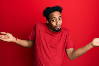 Sakallı, sıradan kırmızı tişörtlü, kafası karışık, elleri ve kolları havada, Afro-Amerikan bir genç. şüphe kavramı. 