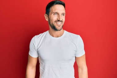 Tişört giyen yakışıklı bir genç. Yan tarafa bakıyor, rahat bir görünüm takınıyor. Kendine güvenen bir gülümsemesi var.. 