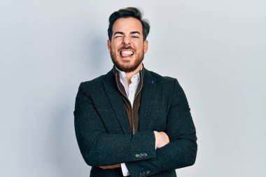 Kollarını kavuşturmuş, sakallı, yakışıklı beyaz adam. Komik bir ifadeyle dilini dışarı çıkarıyor.. 