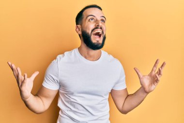 Sakallı, sıradan beyaz tişörtlü genç adam deli gibi bağırıyor, agresif bir ifadeyle bağırıyor ve kollarını kaldırıyor. hüsran kavramı. 