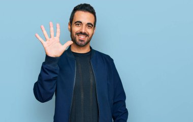 Gündelik kıyafetler giyen genç İspanyol adam beş numarayı gösterip işaret ederken kendinden emin ve mutlu bir şekilde gülümsüyor.. 