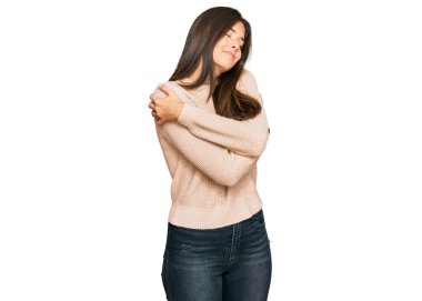 Genç esmer kadın, sıradan bir kazak giyip kendine sarılıyor mutlu ve pozitif, kendinden emin gülümsüyor. Sevgi ve özgüven. 