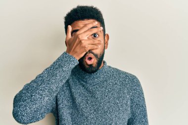 Yakışıklı, sakallı, sıradan kıyafetler giyen, şok içinde yüzünü ve gözlerini kapayarak parmaklarından korkuyla bakan bir İspanyol. 