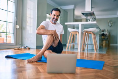 Orta yaşlı, sakallı ve esnek bir adam evde egzersiz yapıyor bilgisayardaki spor videolarına bakıyor.