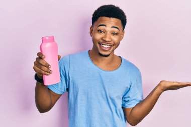 Genç Afrikalı Amerikalı adam elinde şampuan şişesiyle zaferi kutluyor. Gülümsüyor ve ellerini kaldırarak kazanan yüz ifadesi takınıyor. 