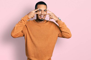 Genç Afro-Amerikan adam günlük kıyafetler giyiyor barış sembolü yapıyor. Yüzünde parmakları var, gülümsüyor ve zaferini gösteriyor. 