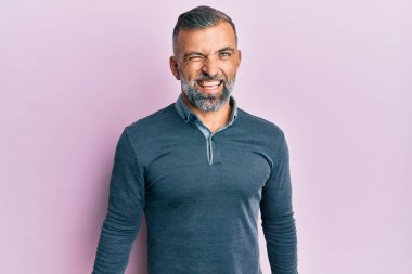 Orta yaşlı, sıradan kıyafetler giyen yakışıklı bir adam kameraya seksi bir ifadeyle bakıyor, neşeli ve mutlu bir yüzle.. 