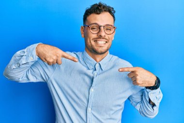 Gündelik kıyafetler ve gözlük takan, kendine güvenen, gülümseyen, kendini gururlu ve mutlu gösteren İspanyol genç bir adam.. 