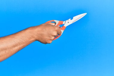 İzole edilmiş mavi arka plan üzerinde makas kullanan genç İspanyol adamın eli..