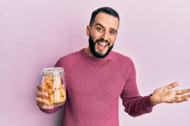 Sakallı genç adam, elinde makarna kavanozuyla zaferi kutluyor. Gülümsüyor ve kazanan yüz ifadesi kaldırıyor. 